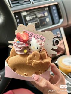 someone holding up a hello kitty ice cream cone with strawberries on top in a car