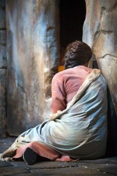 a woman sitting on the ground in front of a stone wall with her back to the camera