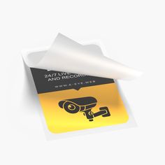 a yellow and black sticker with a camera on it's side next to a roll of white paper