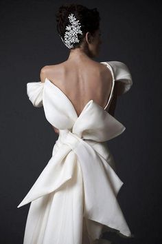 the back of a woman wearing a white dress with a large bow on it's shoulder