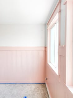 an empty room with pink paint on the walls and blue tape around the window sill