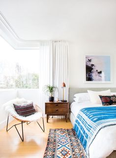 a bedroom with a bed, chair and rug on the wooden floor next to a window