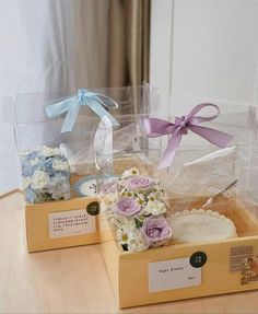 two boxes with flowers in them sitting on a table next to each other and ribbons tied around the lids