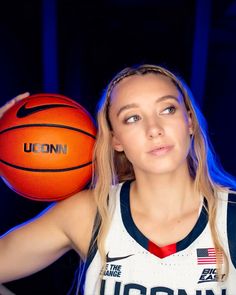 a woman holding a basketball in her right hand and looking at the camera with an intense look on her face