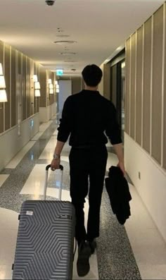 the man is walking down the hallway with his suitcase and bag in hand as he pulls it