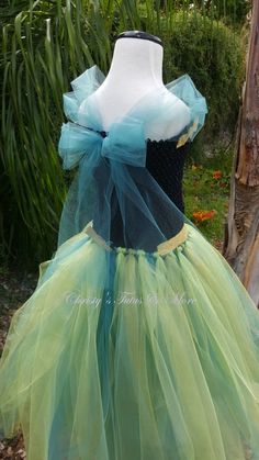 a dress made out of tulle with blue and green ribbons on the top, sitting in front of a tree