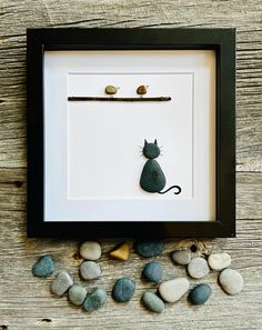 a cat is sitting on the rocks in front of a frame with two little birds perched on it