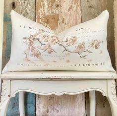 a white bench with a flowered pillow on it's back sitting against a wooden wall