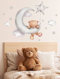 a teddy bear sitting on top of a bed next to the moon and stars wall decal