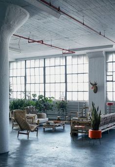 an industrial loft with large windows and lots of furniture on the floor, including couches and chairs