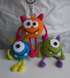 three crocheted toys with eyes and legs on a white surface next to each other