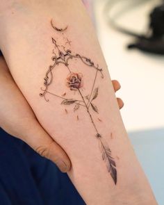 a woman's arm with an arrow and rose tattoo on it