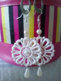 a pair of earrings with white beads hanging from it's earwires on a pink belt