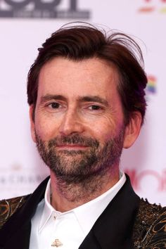 a close up of a person wearing a suit and smiling at the camera with his hair pulled back