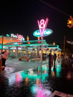 people are walking around in the rain at an outdoor gas station with neon signs and lights