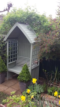 a small garden shed in the middle of some bushes and flowers with yellow flowers around it