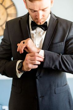 a man in a tuxedo adjusts his watch