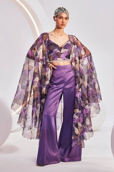 Purple long cape with intertwined floral bloom print. Paired with an inner padded blouse with all over floral bloom print. Paired with a trouser.
Components: 3
Pattern: Print
Type Of Work: Floral Bloom
Neckline: V Neck
Sleeve Type: Sleeveless
Fabric: Blouse: Printed Chiffon, Pant:Heavy Satin, Cape:Printed Organza
Color: Purple
Other Details: 
Attached lining
Blouse:
Padded
Crystal stone lace hem
Occasion: Sangeet - Aza Fashions Printed Organza, Floral Chiffon Blouse, Long Cape, Padded Blouse, Chiffon Floral, Purple Blouse, Lace Hem, Floral Chiffon, Chiffon Blouse