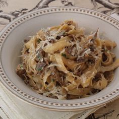 a white bowl filled with pasta and meat on top of a table next to a napkin