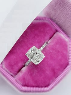 an engagement ring with a princess cut diamond set in a pink velvet box, on display