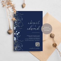 an elegant wedding card with blue flowers and leaves on it, next to a envelope