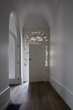 an empty hallway with stained glass windows and wood flooring on either side of the door