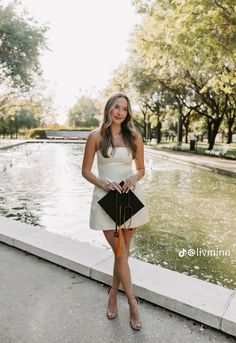 a woman standing in front of a pond holding an orange and black purse with her right hand