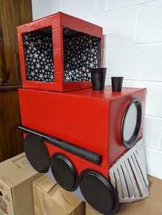 a red toy train sitting on top of cardboard boxes next to a box with black cups