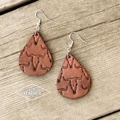 a pair of earrings with an animal design on them sitting on a wooden table next to a piece of wood