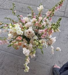 a bouquet of flowers sitting on the ground next to a person's feet in sandals