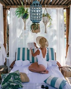 a woman sitting on top of a bed under a canopy next to potted plants