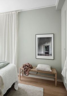 a white bed sitting next to a wooden bench in a bedroom under a painting on the wall