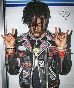 a man with dreadlocks making the peace sign and wearing a jacket that has skulls on it