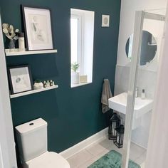 a white toilet sitting next to a bathroom sink under a window in a green wall