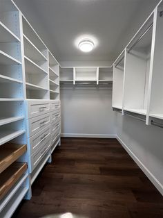 an empty walk in closet with white shelving and wood flooring on the side