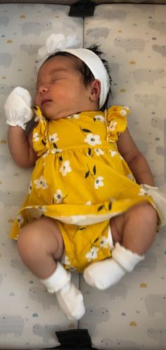 a newborn baby wearing a yellow dress and white headband is sleeping on a bed