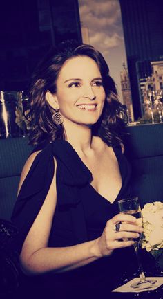 a woman sitting at a table with a glass in her hand and flowers in front of her