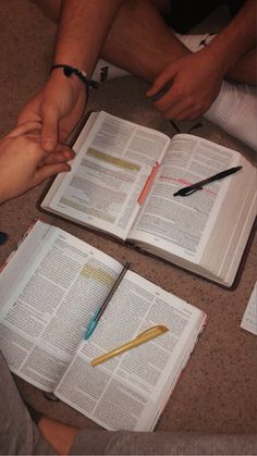 two people sitting at a table holding hands over an open book with writing utensils on it