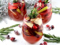 three glasses filled with fruit and veggies on top of a white surface next to evergreen branches