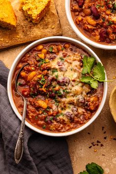 two bowls filled with chili and beans next to bread