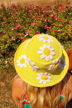 a woman wearing a yellow hat with flowers on it sitting in front of a flower garden