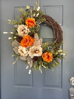 an orange and white wreath is hanging on the front door, with flowers in it