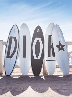 three surfboards sitting on top of each other in front of a fence with the word dior written on it