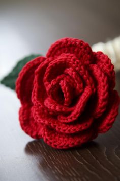 a crocheted red rose sitting on top of a wooden table