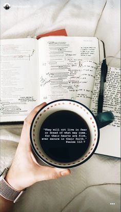 a person holding a cup of coffee in front of an open book with writing on it