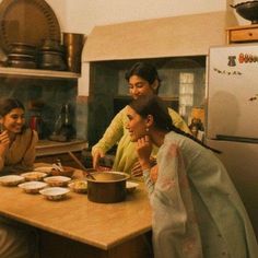 three women sitting at a kitchen table with food in front of them and one woman standing behind the counter