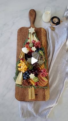 a wooden cutting board topped with fruit and cheese on top of a white tablecloth