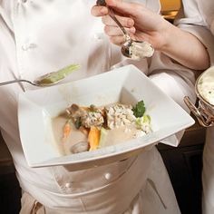 a woman in a chef's uniform holding a plate with food on it