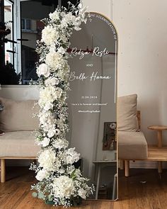 a wedding arch with white flowers and greenery in front of a mirror on the floor