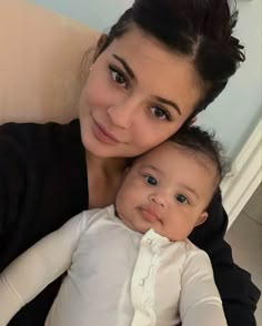 a woman holding a baby in her arms and looking at the camera while sitting on a couch